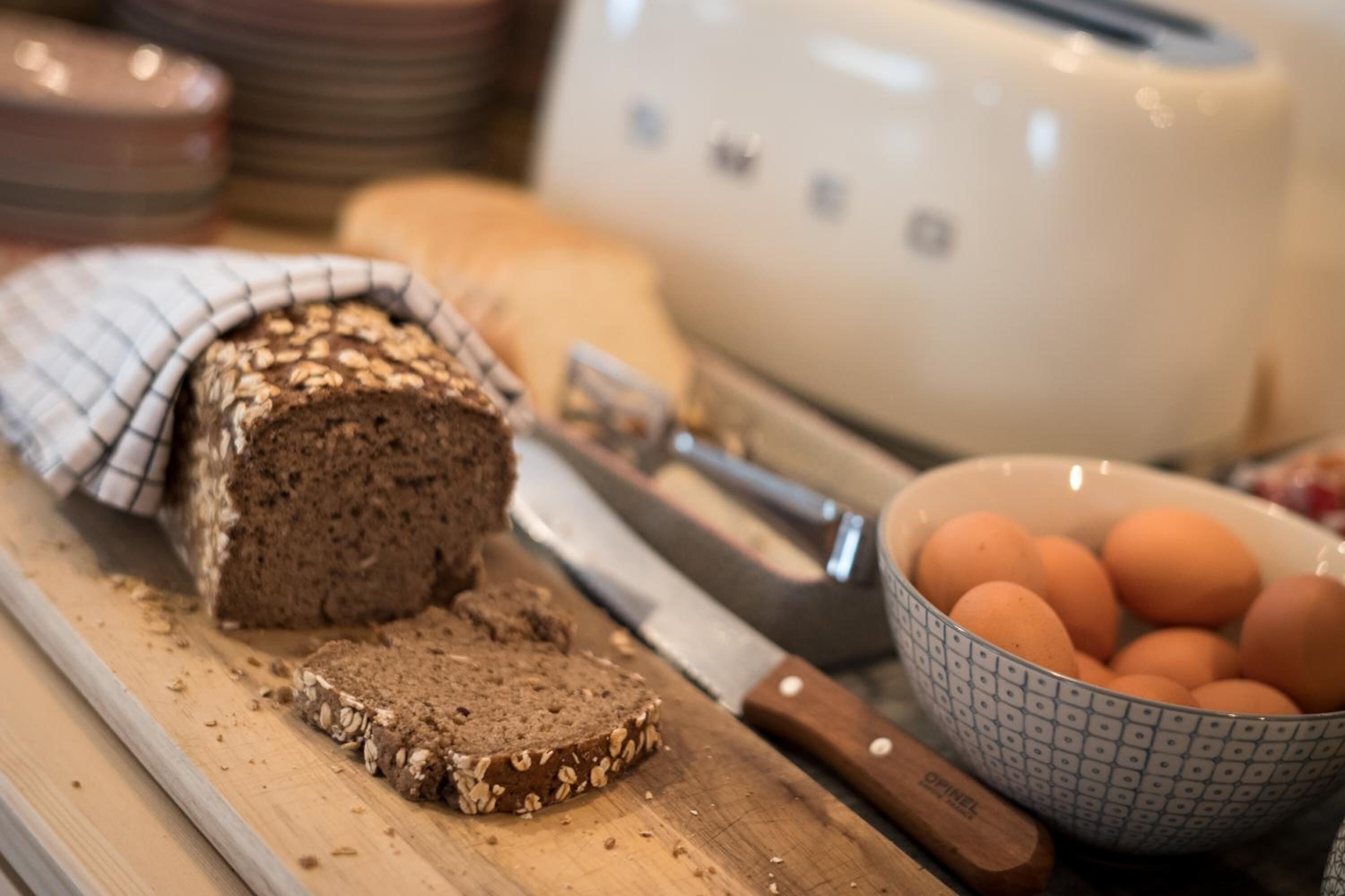 A loaf of bread on a cutting board, a knife, and a bowl of eggs.