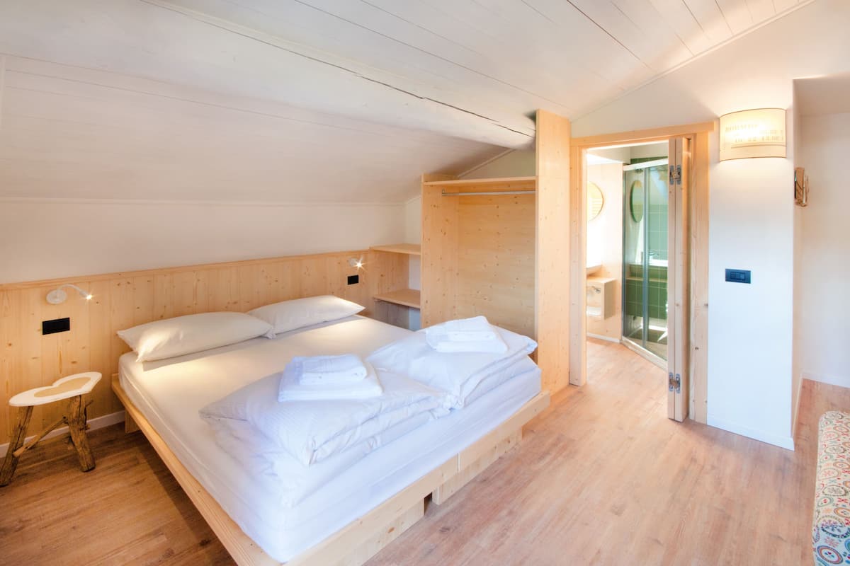 A wooden-paneled bedroom with a bed, a small bedside table, and a door leading to a bathroom.