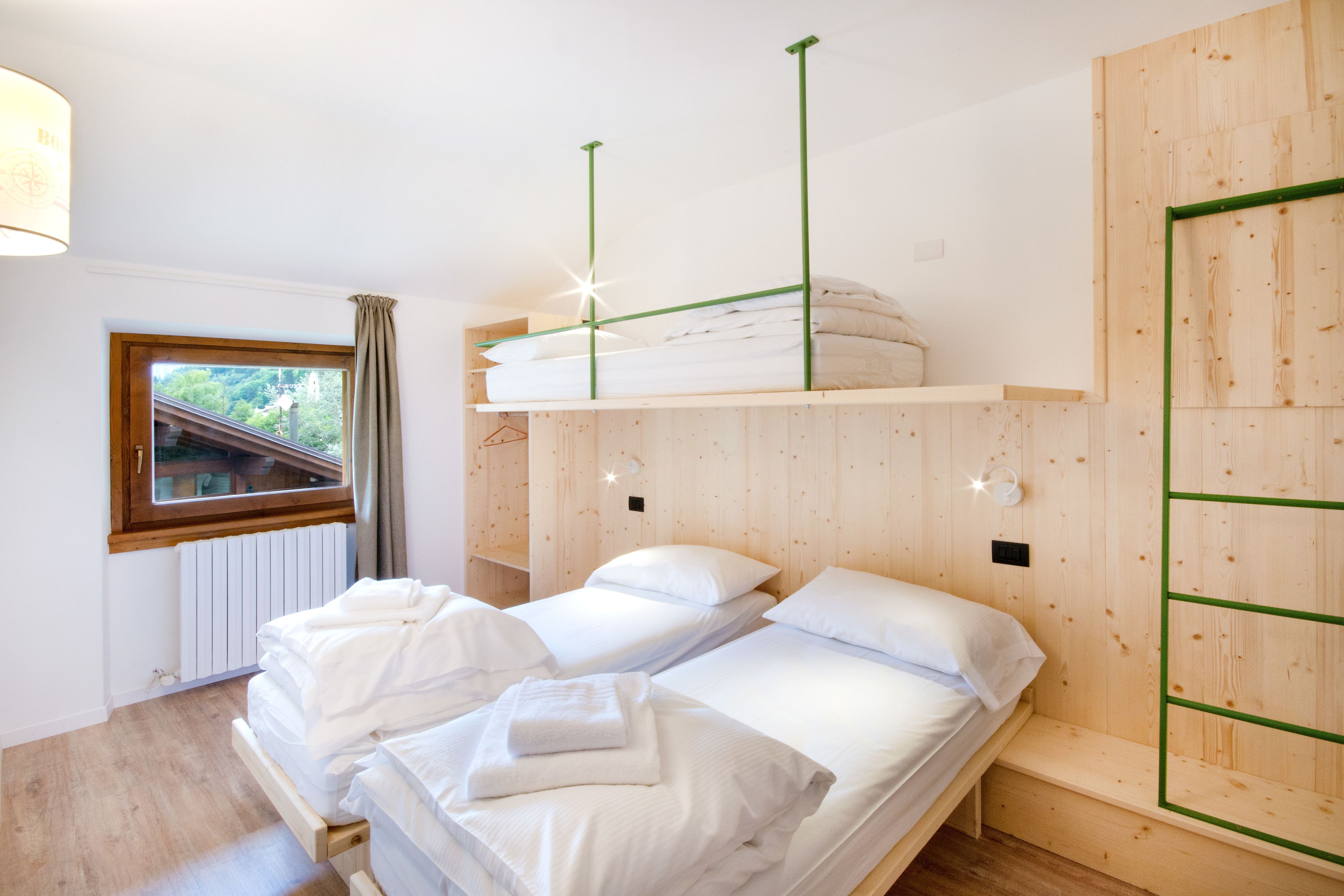 Una habitaci ón con dos camas, una ventana con vistas, paredes de madera y un estante colgante sobre las camas.