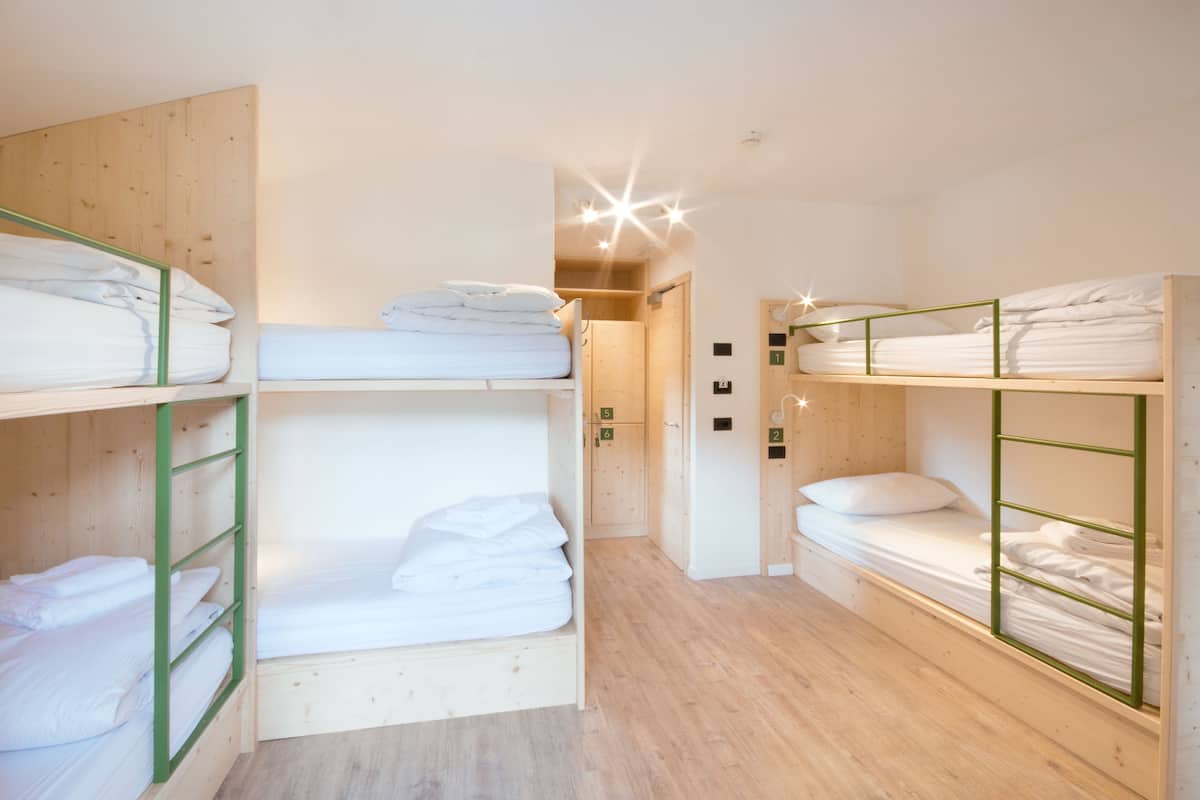 A dormitory room with bunk beds, wooden walls, and a hallway leading to a bathroom.