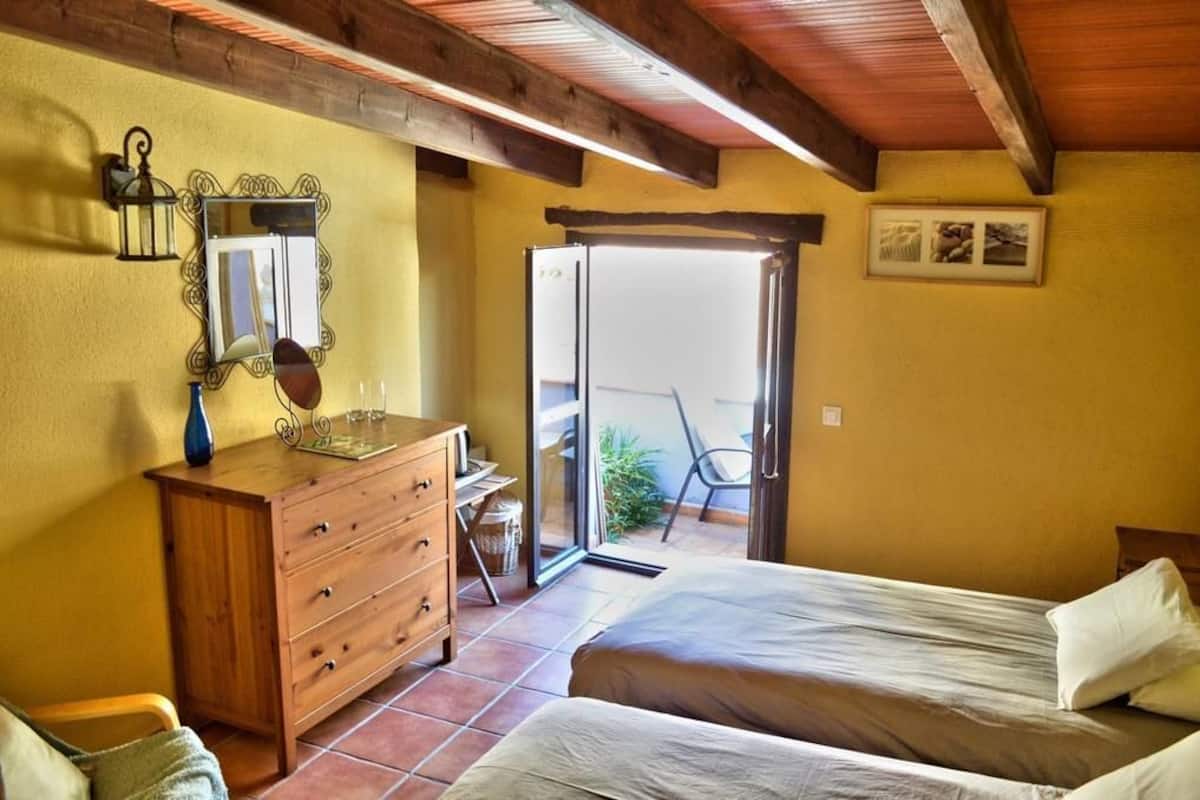 Un dormitorio con dos camas, un aparador de madera, un espejo y una puerta corrediza de vidrio que da a un espacio exterior.