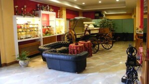 A spacious living room with a leather sofa, a vintage carriage, and a display cabinet with trophies. - Hotel Residence Memmina (Frosinone)