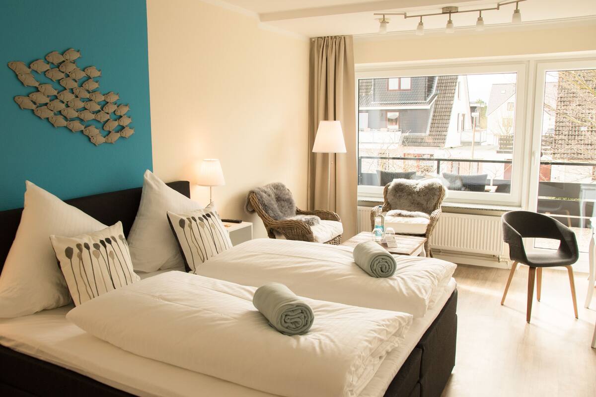 A hotel room with a large bed, two bedside tables, a chair, a window with a view of buildings, and a wall decoration.