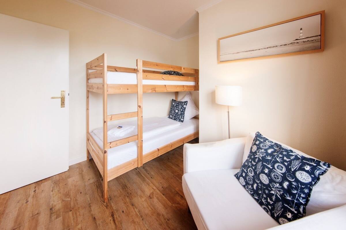 A room with a bunk bed, a white sofa with patterned cushions, a framed picture on the wall, and a floor lamp.