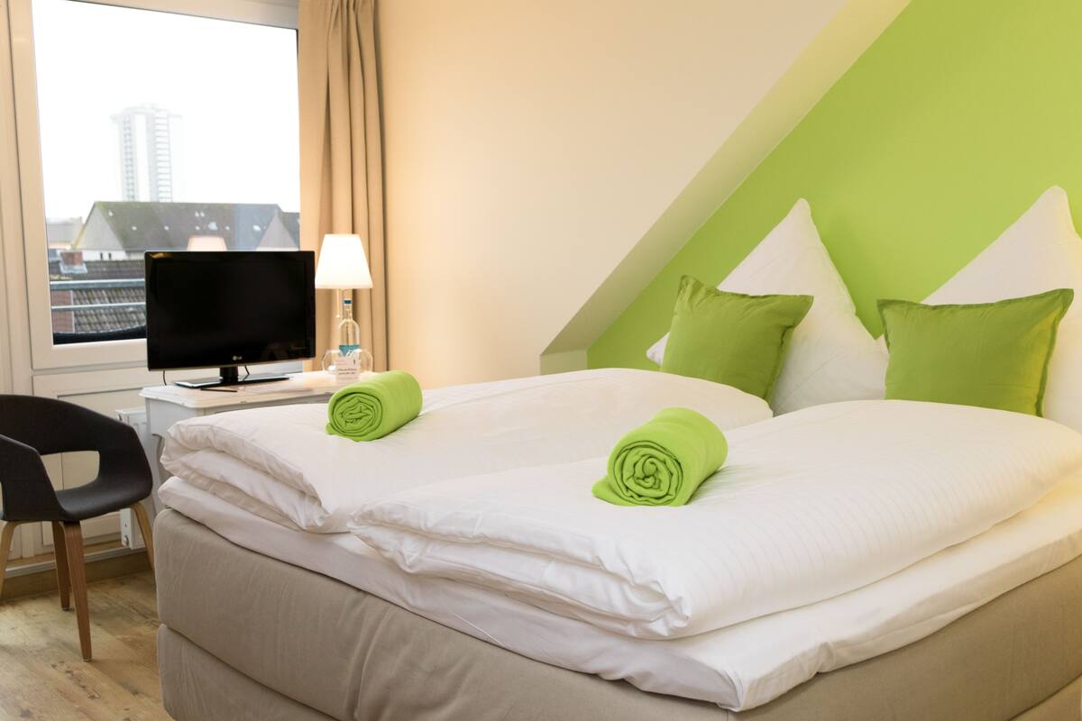 A hotel room with two beds, a desk with a computer, a chair, and a TV.