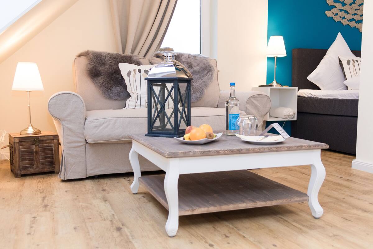 A modern living room with a sofa, a coffee table with fruit, a lamp, and a decorative wall piece.