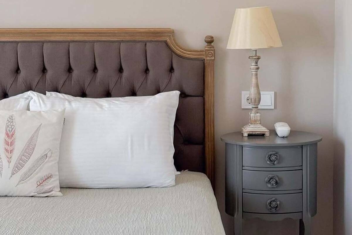 A bedroom with a tufted headboard, a bedside table with a lamp, and a bed with a white pillow.
