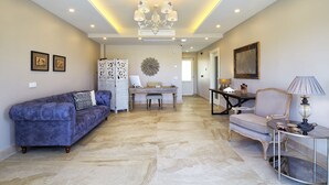 A spacious living room with a blue sofa, a wooden dining table, and a chandelier.