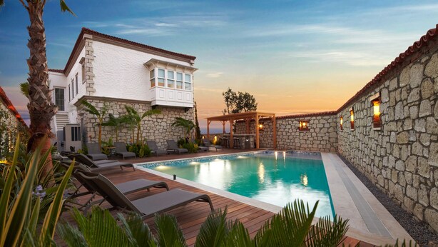 A pool area with lounge chairs, a pergola, and stone walls.
