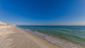 A beach with a clear sky, calm sea, and buildings in the background. - Seaside Beach & Racquet 5614 (Orange Beach)