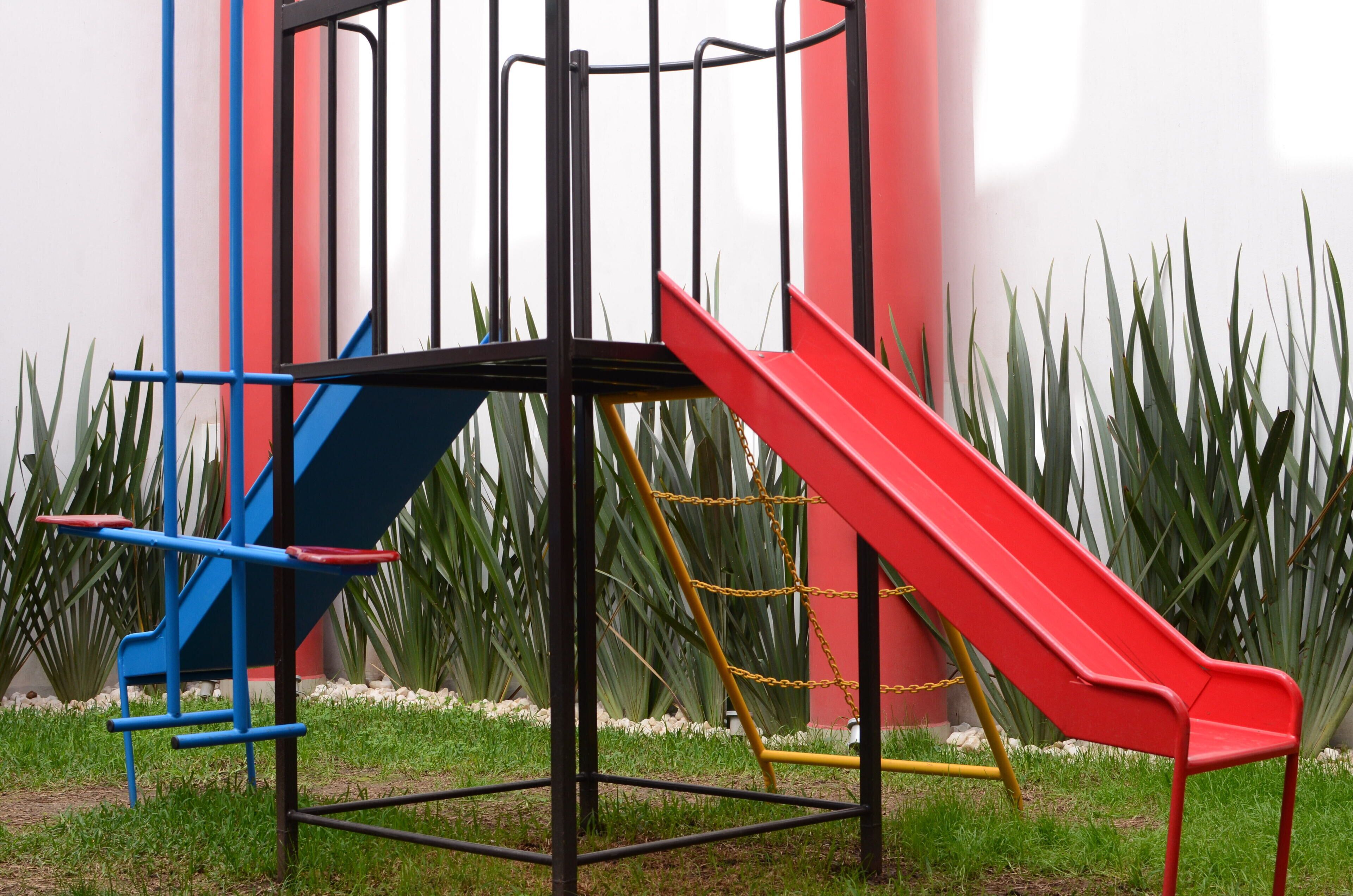 A playground with a red slide and blue climbing structure.