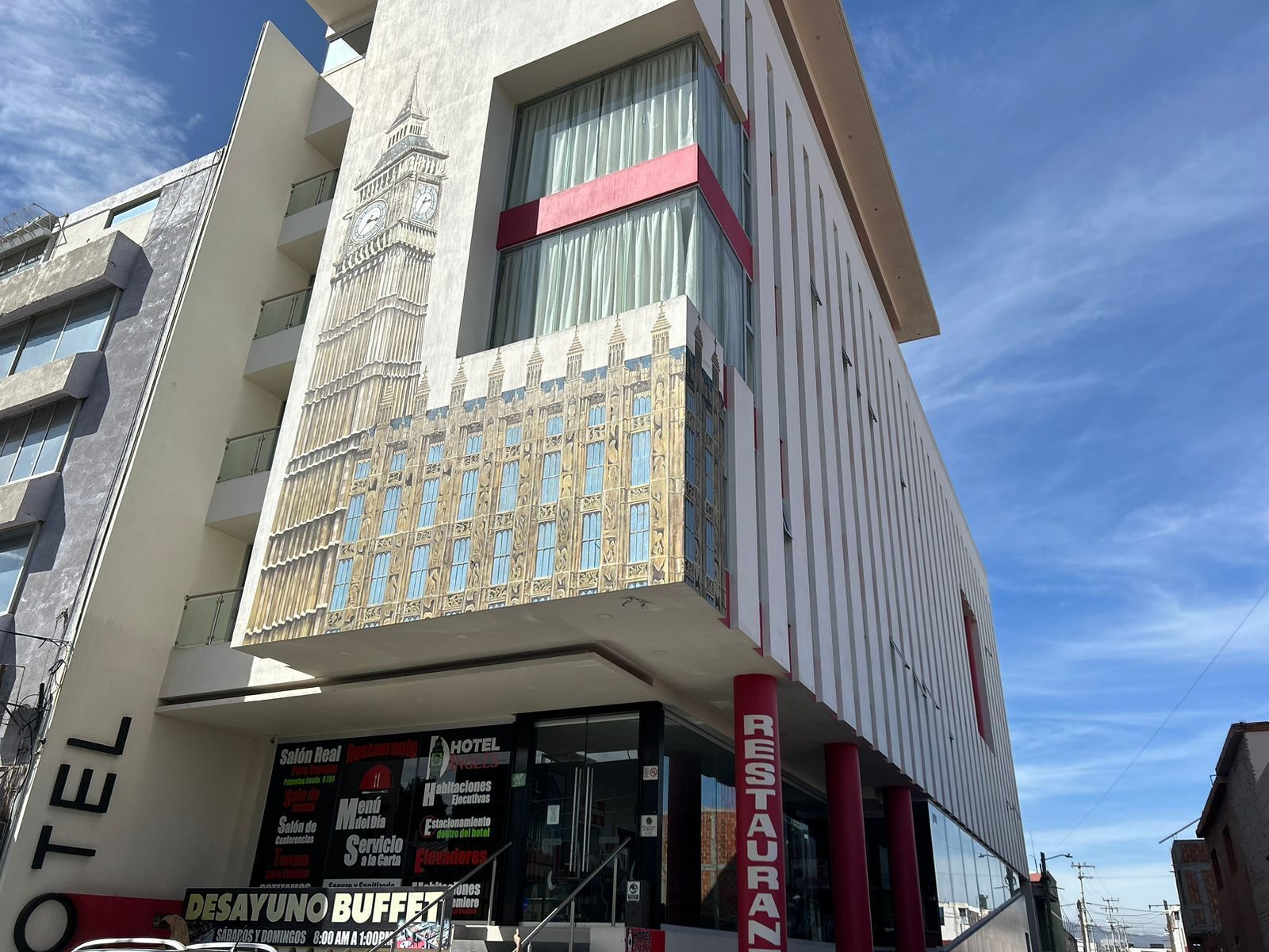 Un hotel con una imponente fachada de torre con reloj, un letrero de restaurante y un letrero de bufé.