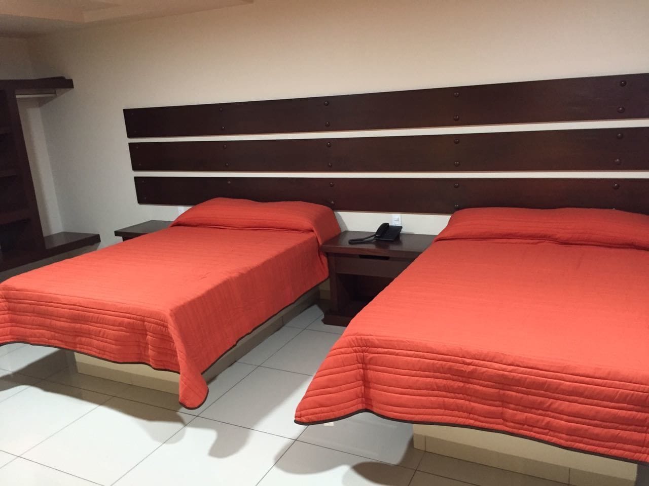 Une chambre avec deux lits, chacun recouvert d’une couverture rouge et doté d’une tête de lit en bois. Une table de chevet avec un téléphone est placée entre les deux lits.
