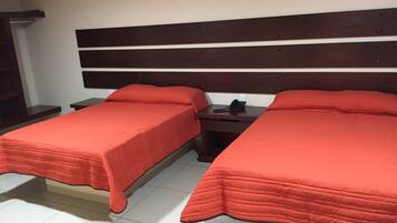Une chambre avec deux lits, chacun recouvert d’une couverture rouge et doté d’une tête de lit en bois. Une table de chevet avec un téléphone est placée entre les deux lits.