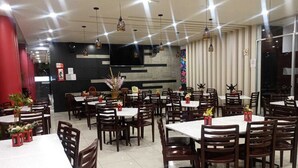 Ein Restaurant mit mehreren Tischen, Stühlen, einer Küchenzeile und hängenden Pendelleuchten.