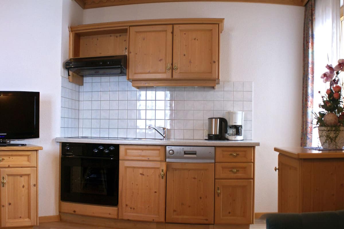 A compact kitchen with wooden cabinets, a built-in oven, and a dining area with a table and chairs.