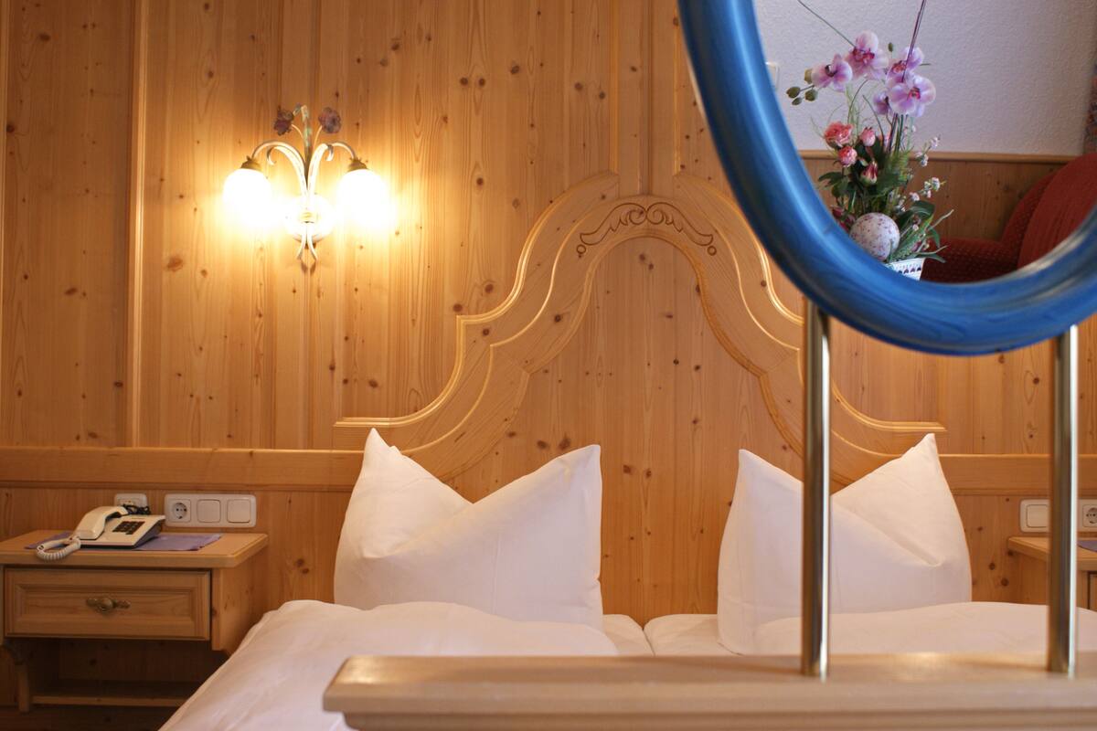 A wooden-paneled room with a bed, a nightstand with a telephone, and a wall-mounted light fixture.
