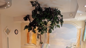 A sunlit room with reclining chairs, a large plant, and a mural of a landscape. - Sportapart Mallaun (See)