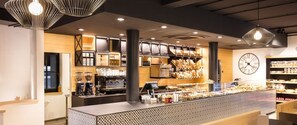 A bakery counter with a variety of baked goods, a coffee machine, and a clock on the wall. - Sportapart Mallaun (See)