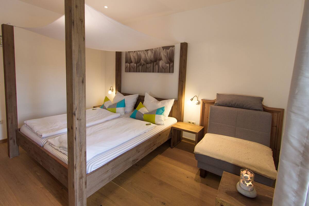 Un dormitorio con cama de madera, una mesita de noche, una silla y una obra de arte en la pared.