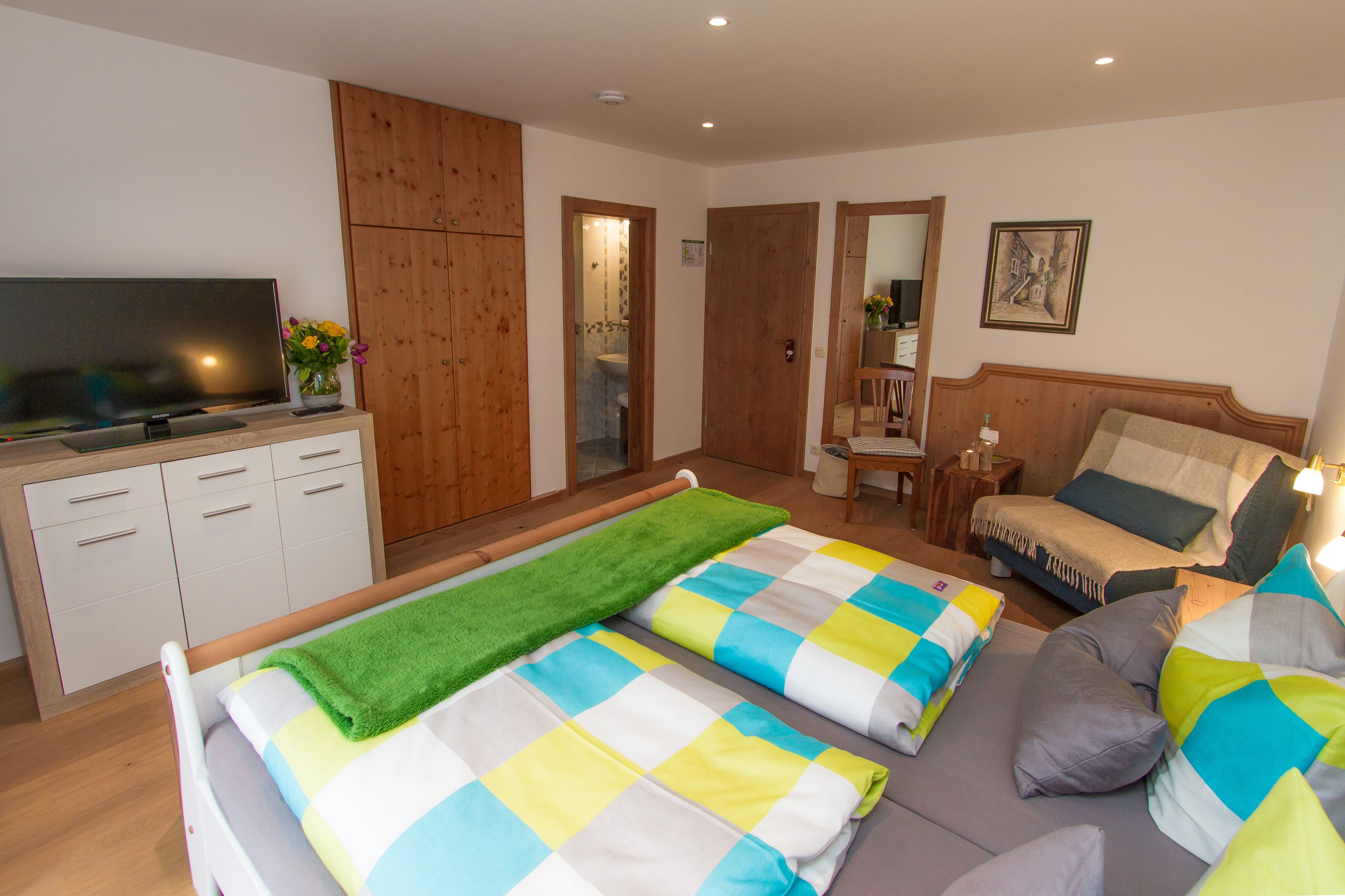 A modern bedroom with a bed, a sofa, a TV, and a wooden wardrobe.