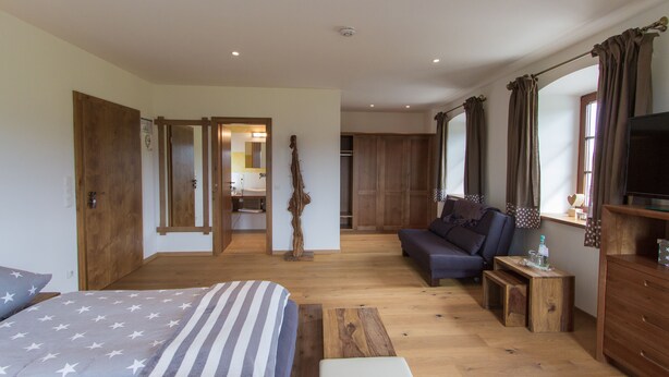Une chambre à coucher avec un lit, un canapé, une télévision et une commode en bois.