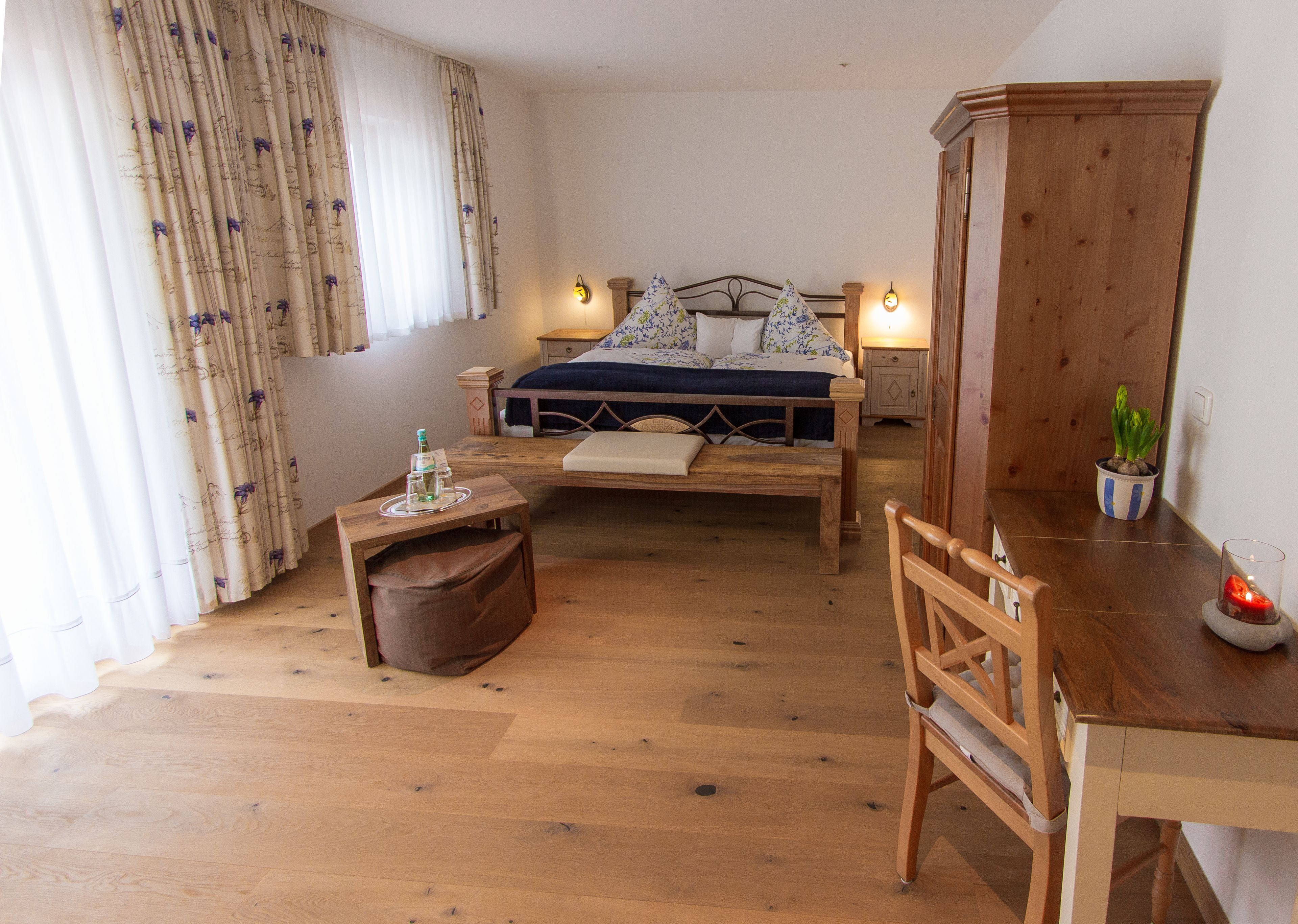 A bedroom with a wooden bed, bedside tables, a small table with a candle, a chair, and a potted plant.