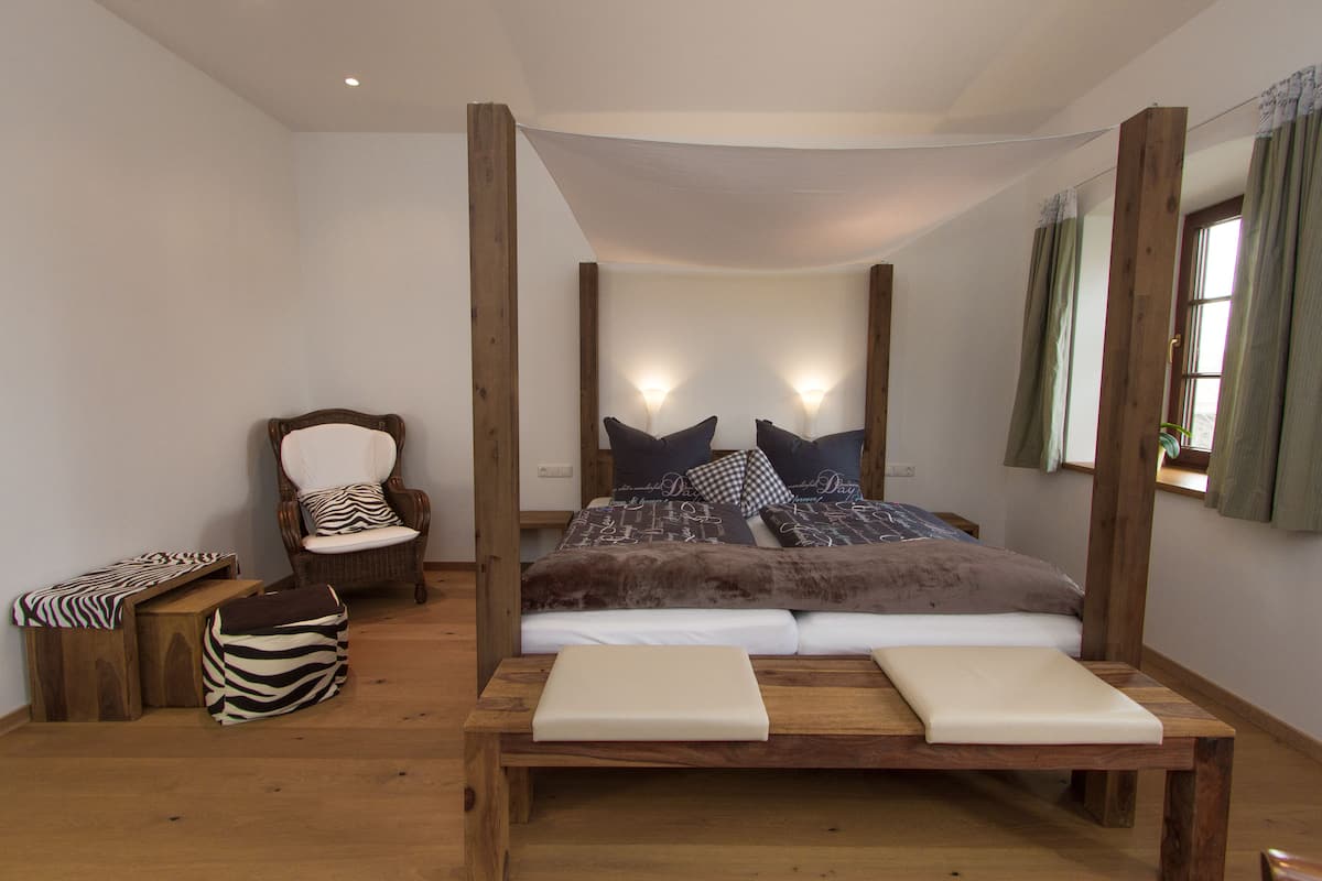 Un dormitorio con cama con dosel, un banco de madera, una silla y un reposapiés estampado con motivos de cebra.
