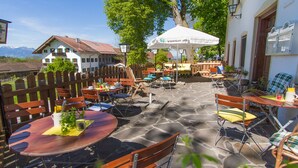 Une terrasse extérieure avec des tables et des chaises en bois, un sol en pierre et un parasol blanc.