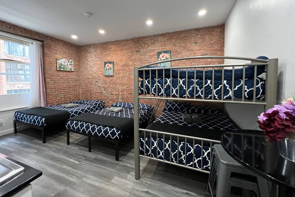 Dormitorio con literas, pared de ladrillo, dos ventanas y una pequeña cocina.