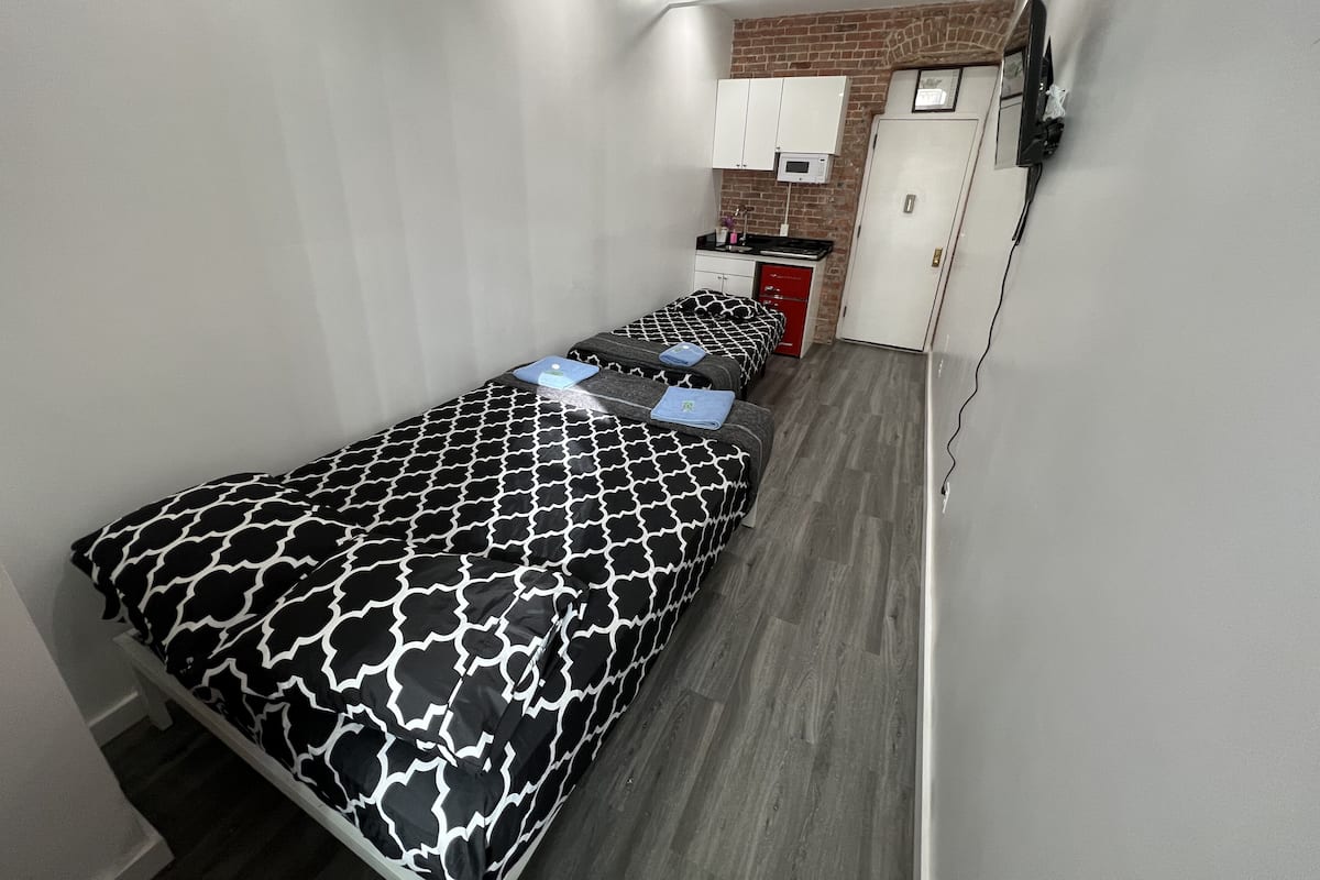 Una habitación pequeña con una cama, un rincón de cocina y una puerta.