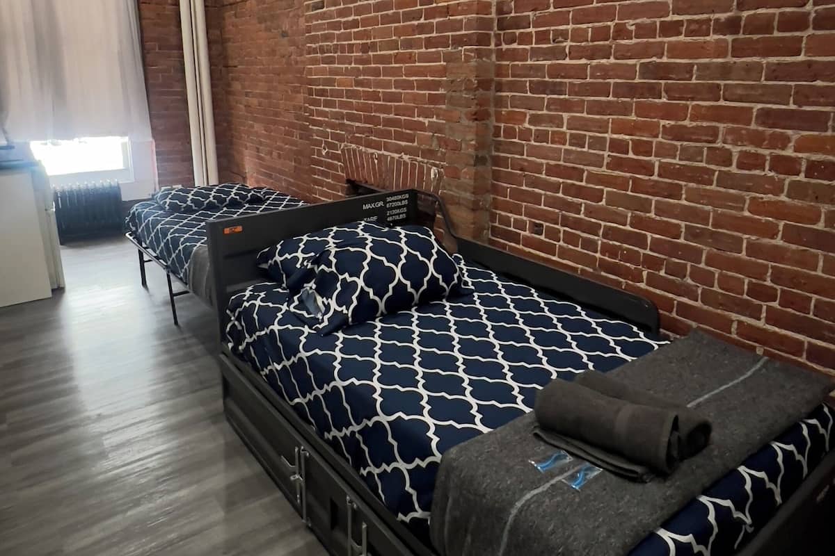 Una habitación con pared de ladrillo, cama con colcha estampada, radiador y ventana con cortinas.