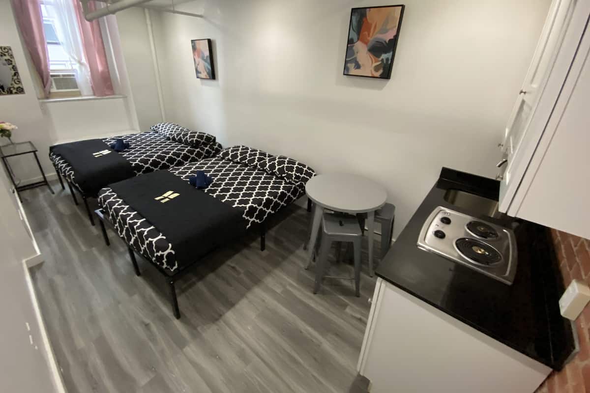 Habitación pequeña con dos camas, una mesita y kitchenette.