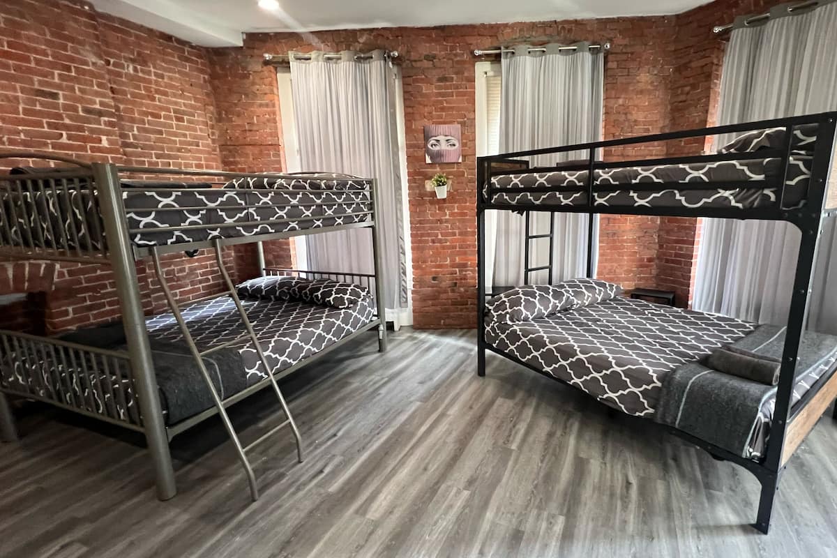 Una habitación con dos literas, una pared de ladrillo y una ventana con cortinas.