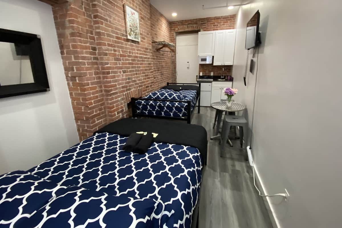 Una habitación compacta con dos camas, una kitchenette pequeña y un televisor en la pared.