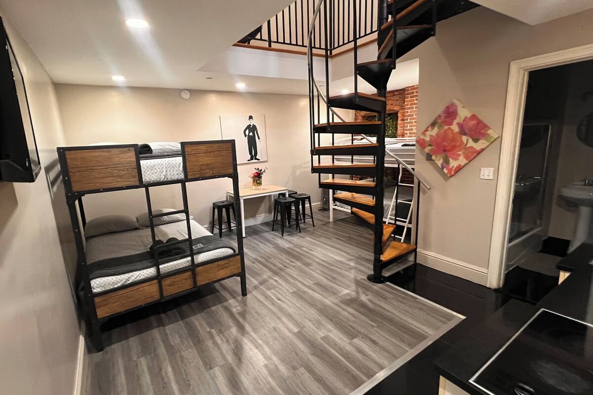 Una habitación pequeña con literas, una mesita y una escalera.