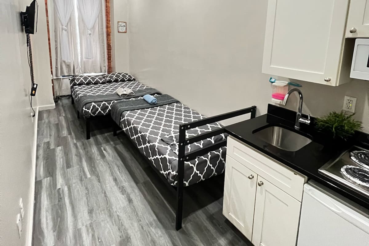 Una habitación compacta con cama, una pequeña kitchenette y un baño con cortina de ducha.