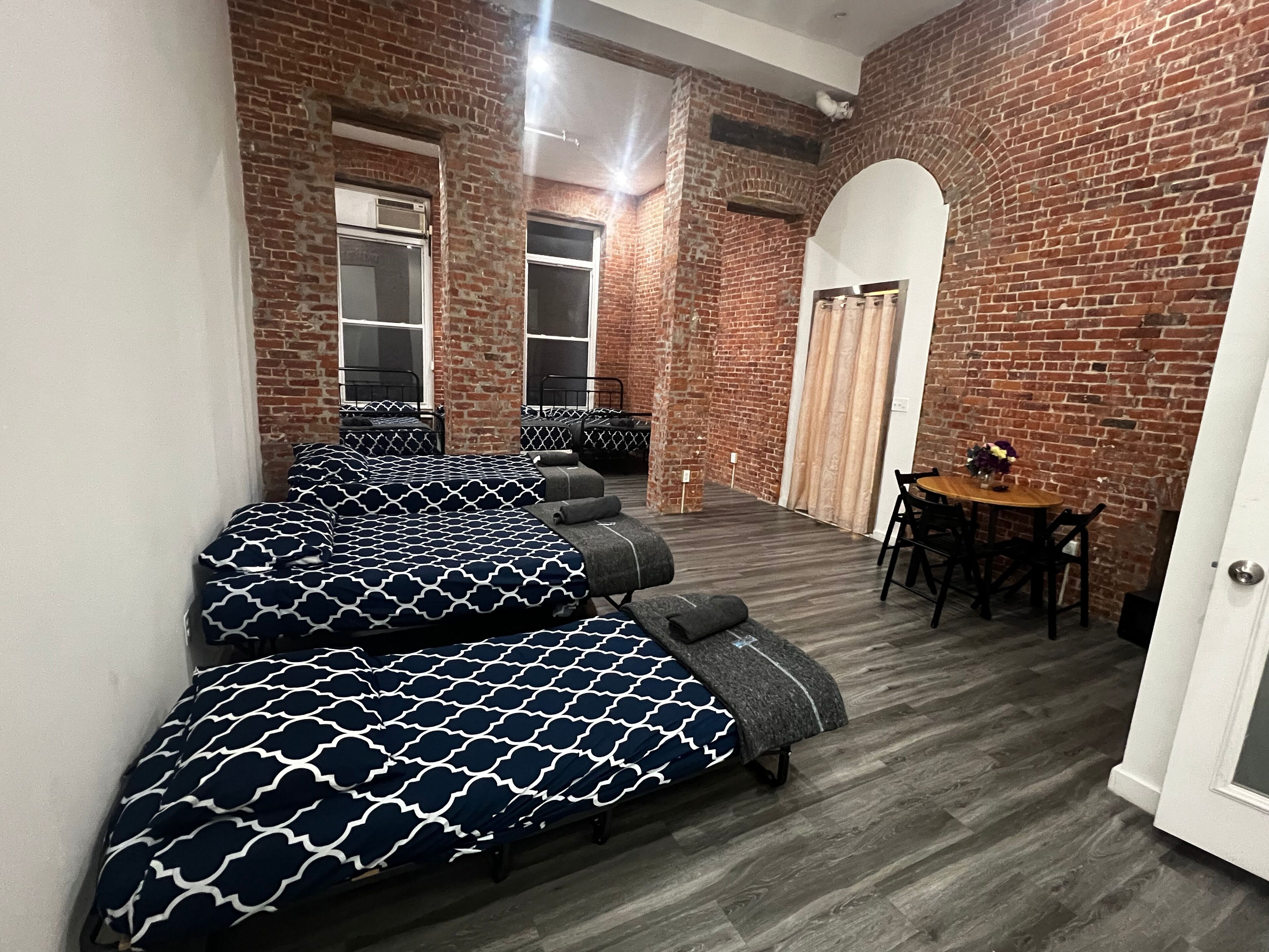A room with two beds, a wooden table, and a brick wall.