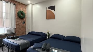 A room with two beds, a brick wall, a green wreath, a painting, and a small table with a lamp.