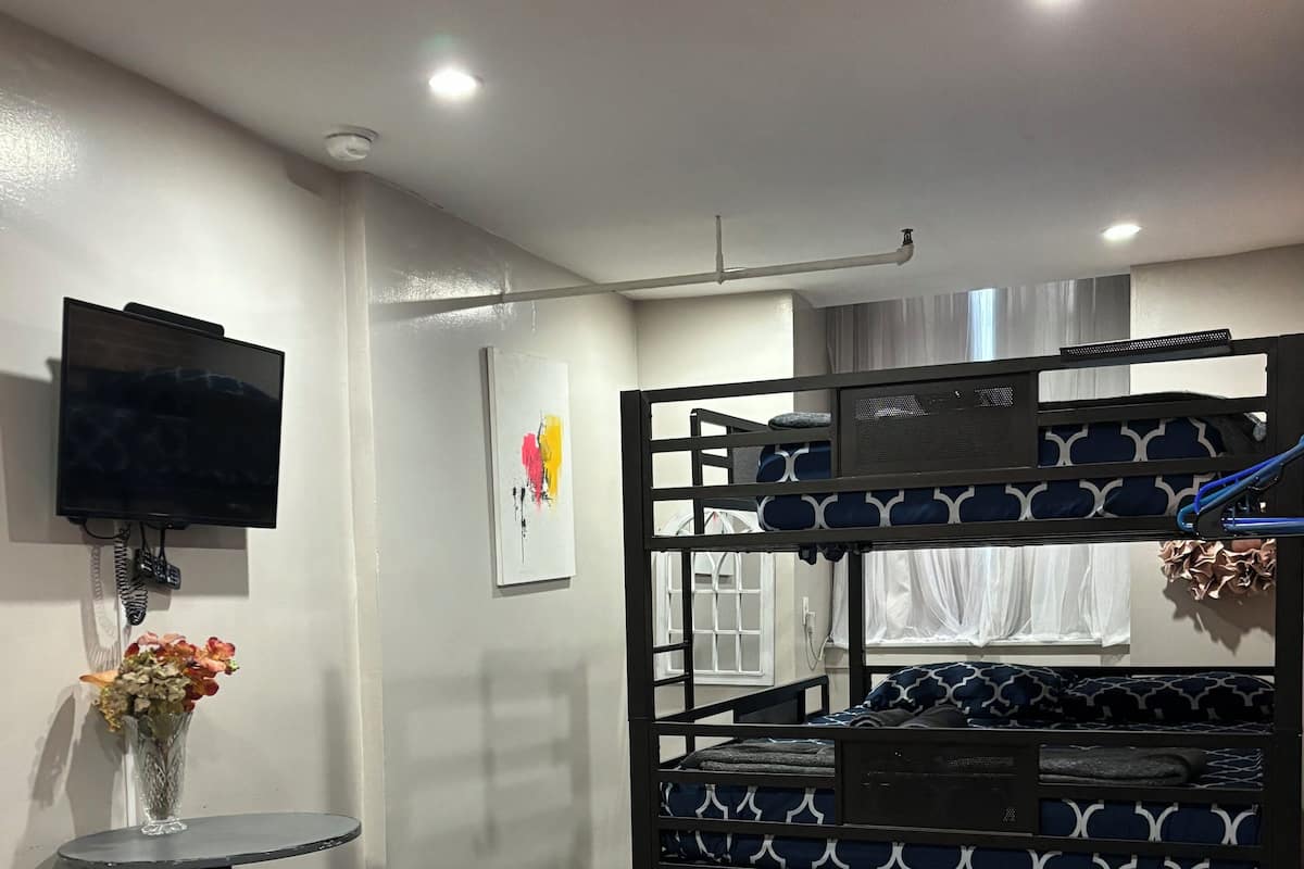 Una cama tipo litera con un televisor en la pared, una mesita con taburetes y un jarrón con flores.