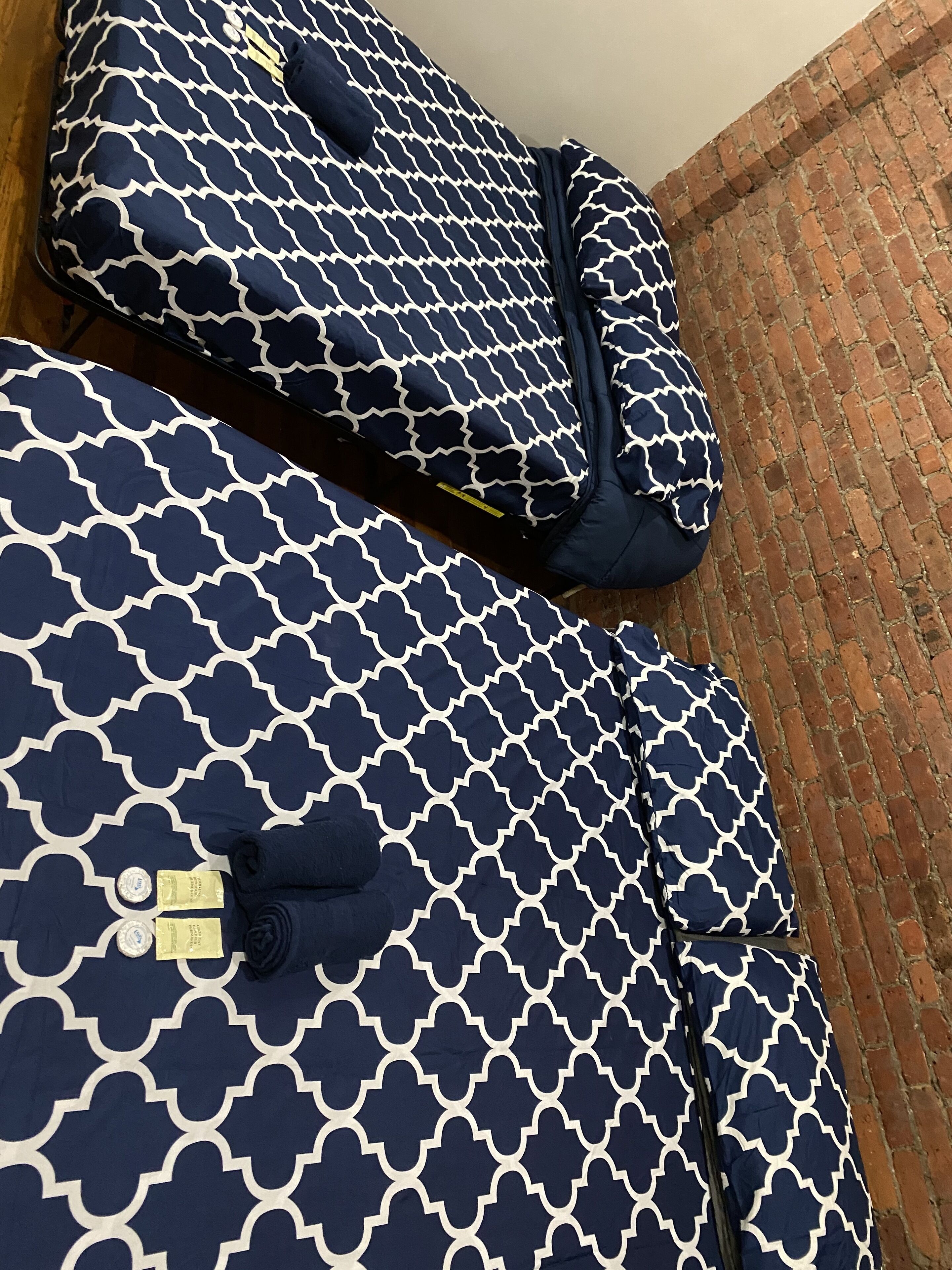 A room with two large, navy blue patterned suitcases with gold accents, a brick wall, and a wooden floor.