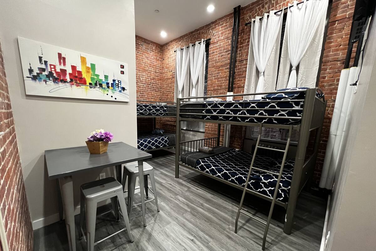 Un dormitorio con literas, una mesita con una silla y un cuadro de un paisaje urbano en la pared.
