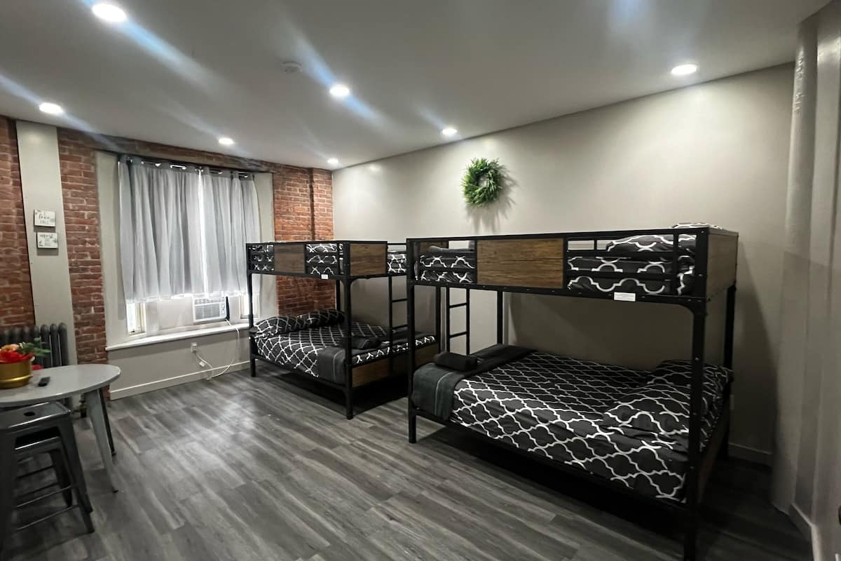 Habitación tipo dormitorio con literas, una mesita pequeña y una ventana con cortinas.
