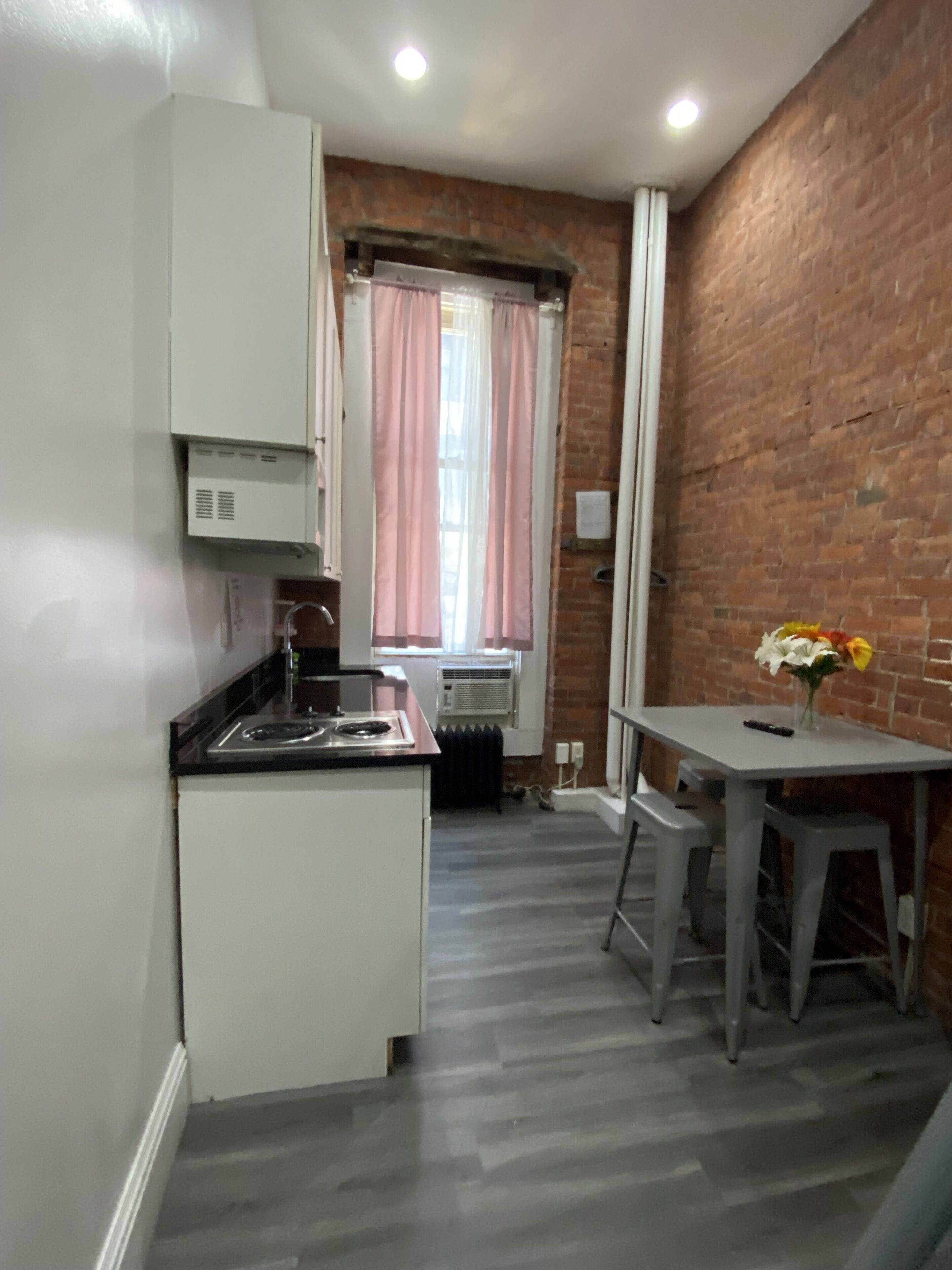 Uma cozinha compacta com armários brancos, bancada preta e janela com cortinas cor-de-rosa.