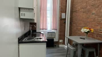Uma cozinha compacta com armários brancos, bancada preta e janela com cortinas cor-de-rosa.
