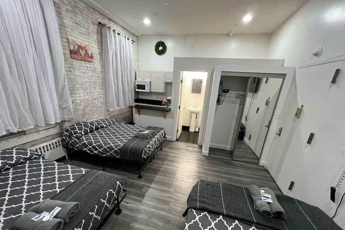 Una habitación con dos camas, una kitchenette pequeña, un baño y un armario.