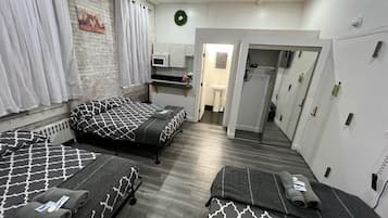 A room with two beds, a small kitchenette, a bathroom, and a wardrobe.