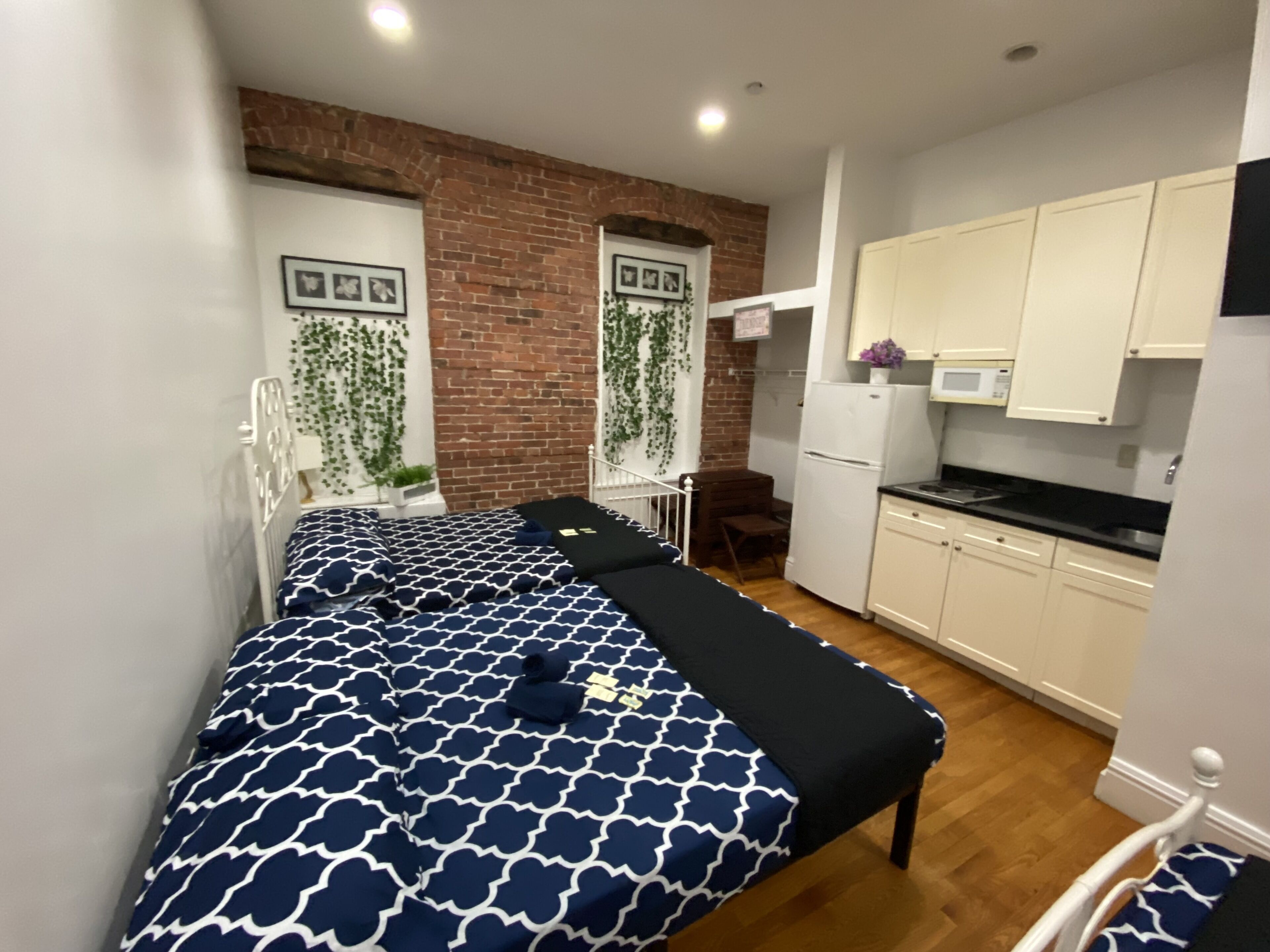 A compact bedroom with a bed, a small desk, and a kitchenette.