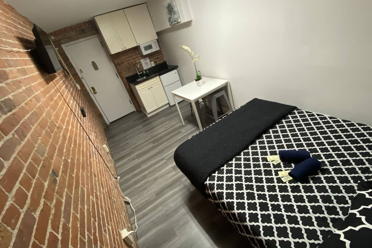 Una habitación pequeña con cama, un escritorio y kitchenette.