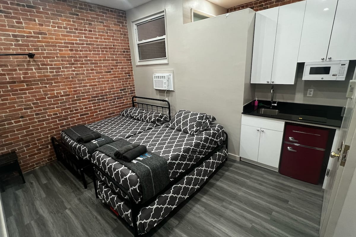 Habitación compacta con cama, kitchenette pequeña y pared de ladrillo.